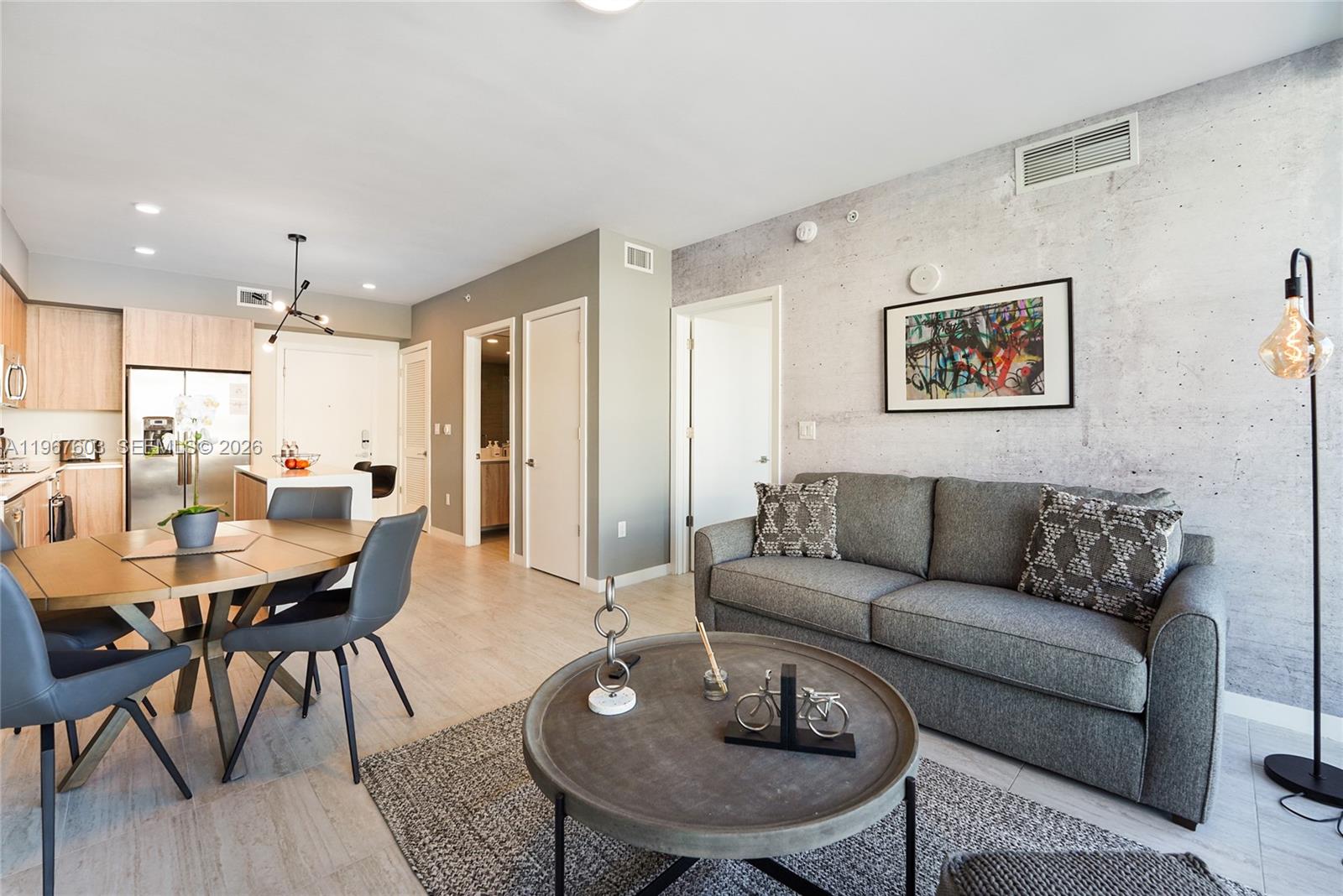 An open-concept living and dining area features a concrete accent wall and modern furniture — 3900 Biscayne Blvd # 218, Miami FL 33137, MIAMI, FL