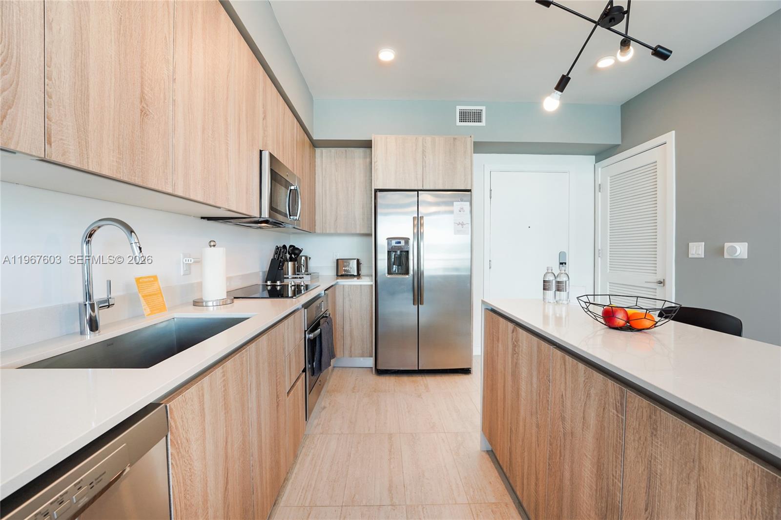 A modern kitchen features light wood cabinetry, stainless steel appliances, and a white quartz island — 3900 Biscayne Blvd # 218, Miami FL 33137, MIAMI, FL