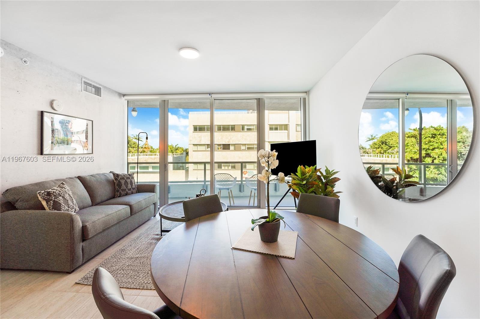 A living and dining area features a gray sofa, round wooden table, and balcony access — 3900 Biscayne Blvd # 218, Miami FL 33137, MIAMI, FL