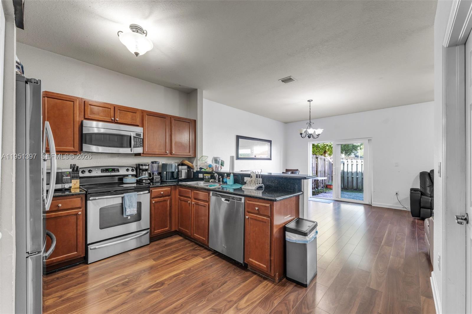 A kitchen with wood cabinets, stainless steel appliances, and dark countertops opens to a living area — 22412 SW 89th Ave, Cutler Bay FL 33190, CUTLER BAY, FL