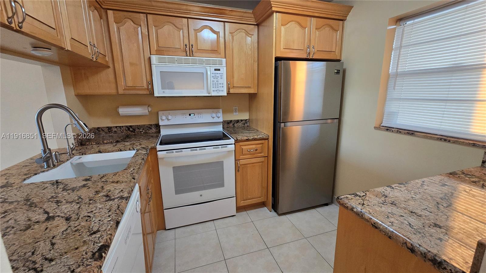 A kitchen features light wood cabinets, granite countertops, a white stove, and stainless steel refrigerator — 9230 Lagoon Pl # 310, Davie FL 33324, DAVIE, FL