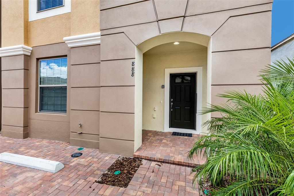 The exterior of a home features a black front door, tan stucco walls, and pavers — 8887 GENEVE COURT, KISSIMMEE, FL