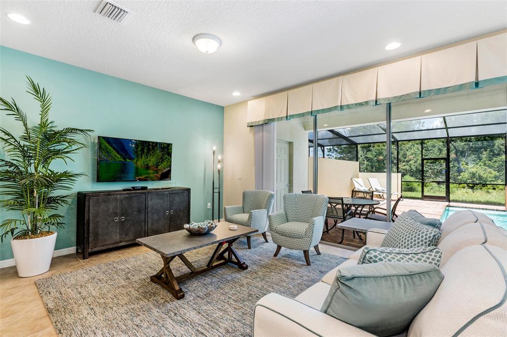 A living room features a teal accent wall, a television, seating, and a screened-in pool — 8887 GENEVE COURT, KISSIMMEE, FL
