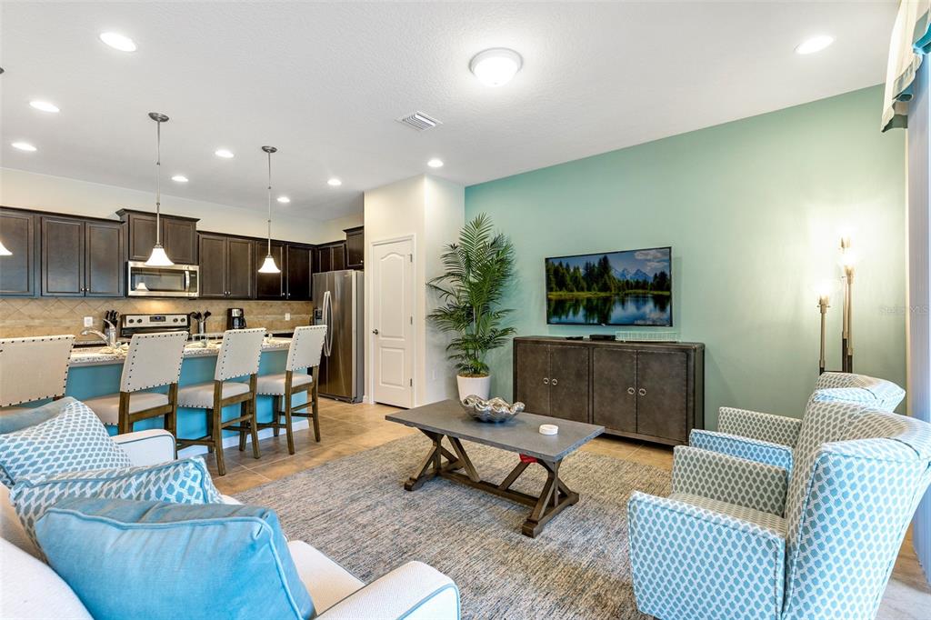 A living room with a teal accent wall, television, and an open kitchen with bar seating — 8887 GENEVE COURT, KISSIMMEE, FL