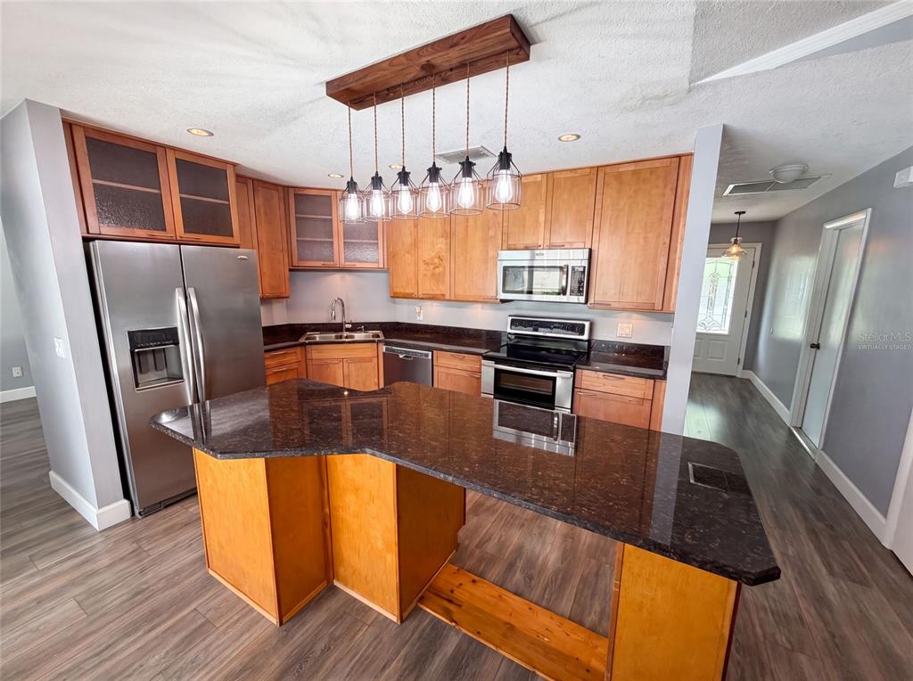 A kitchen features wood cabinets, dark granite countertops, stainless steel appliances, and a pendant light fixture — 4830 DUNBARTON DRIVE, ORLANDO, FL