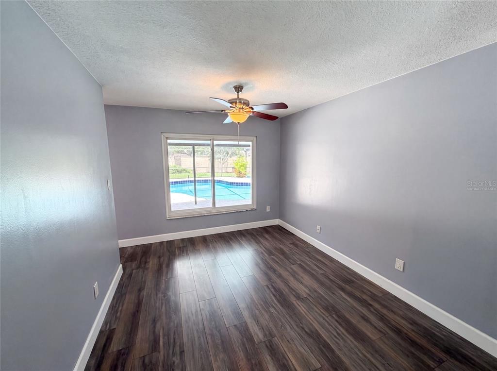 An empty room with gray walls, dark wood-look flooring, a ceiling fan, and a pool view — 4830 DUNBARTON DRIVE, ORLANDO, FL