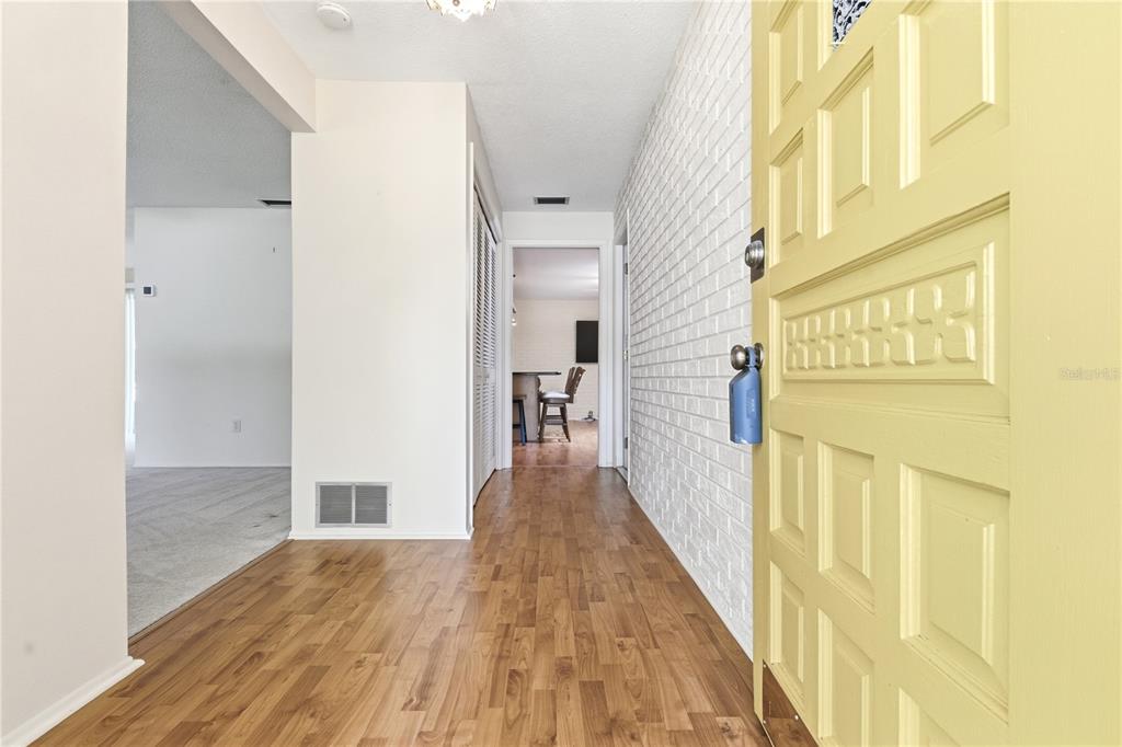 An entryway with wood-look flooring, a yellow front door, and a white brick wall — 1904 GRANADA COURT, CLEARWATER, FL