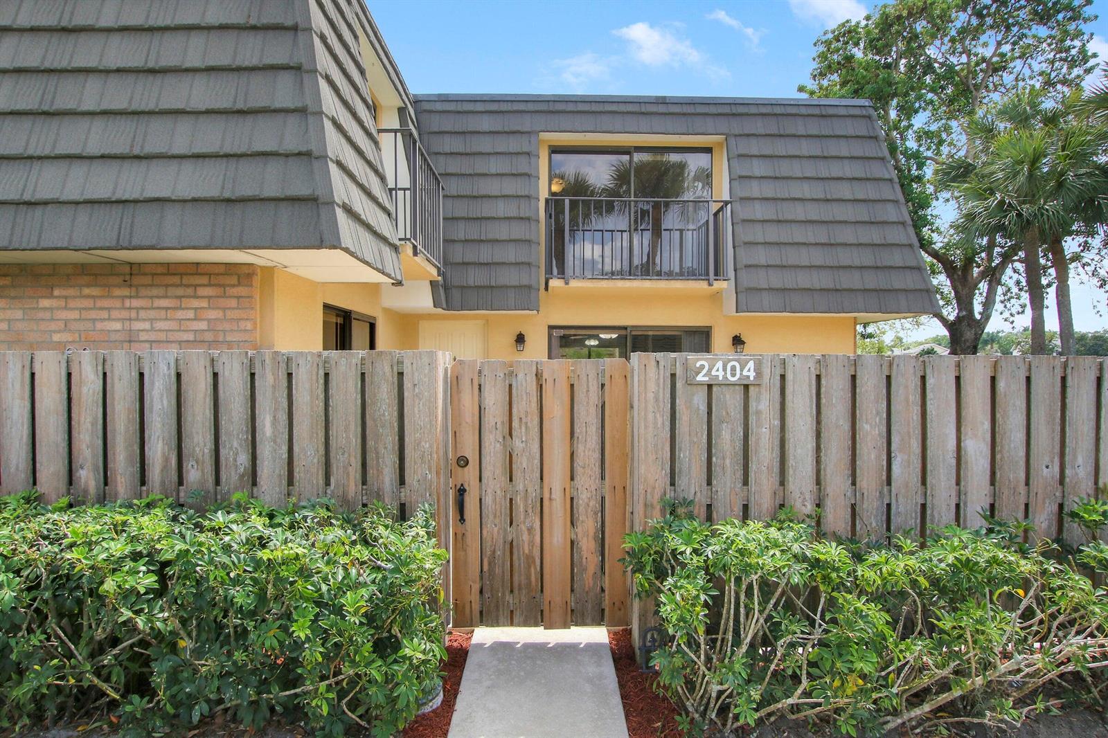 A two-story building exterior features a wooden privacy fence, a gated entrance, and balconies — 2404 24th Way, West Palm Beach FL 33407, WEST PALM BEACH, FL