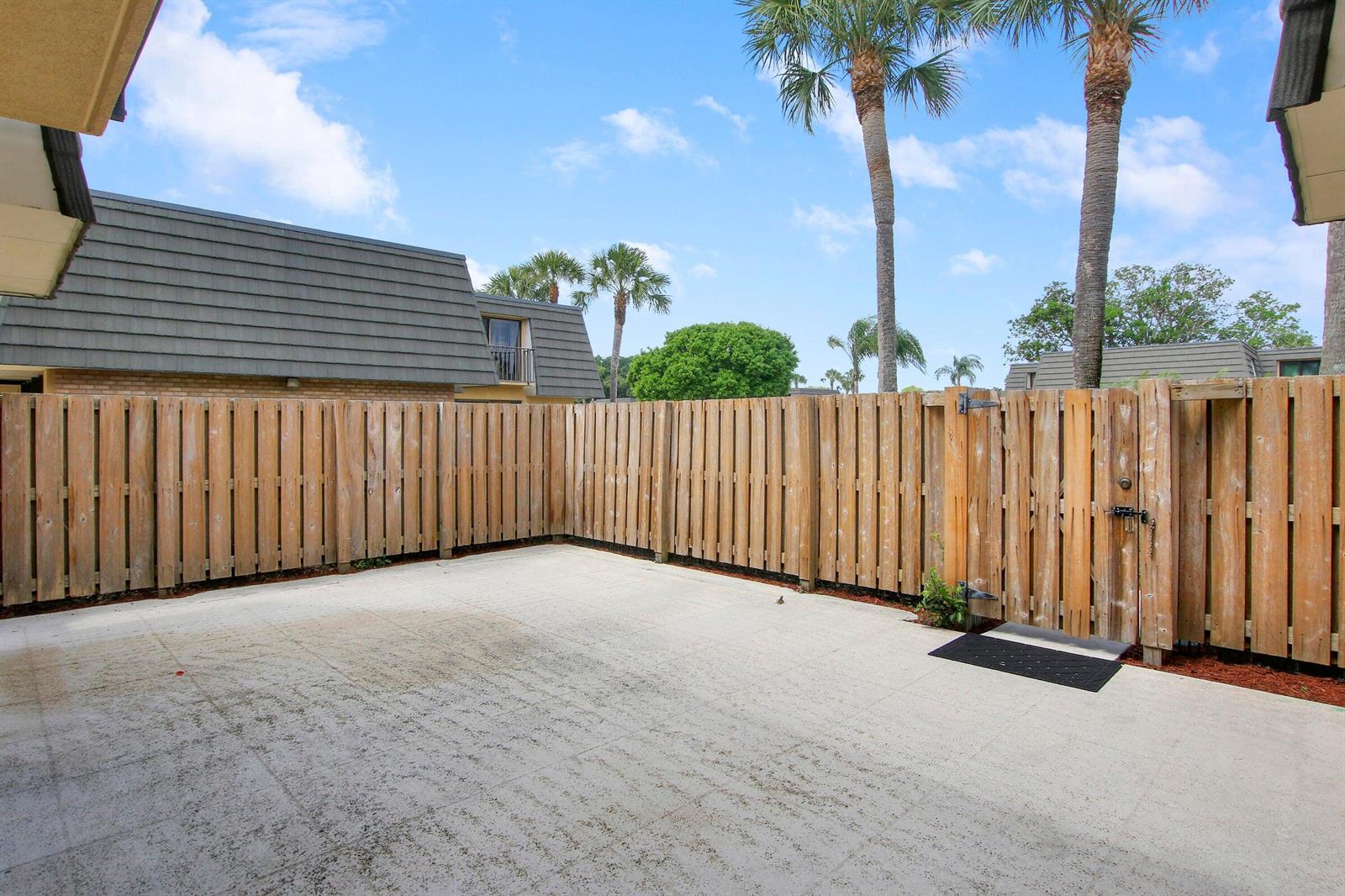 A concrete patio enclosed by a wooden privacy fence with a gate and palm trees — 2404 24th Way, West Palm Beach FL 33407, WEST PALM BEACH, FL