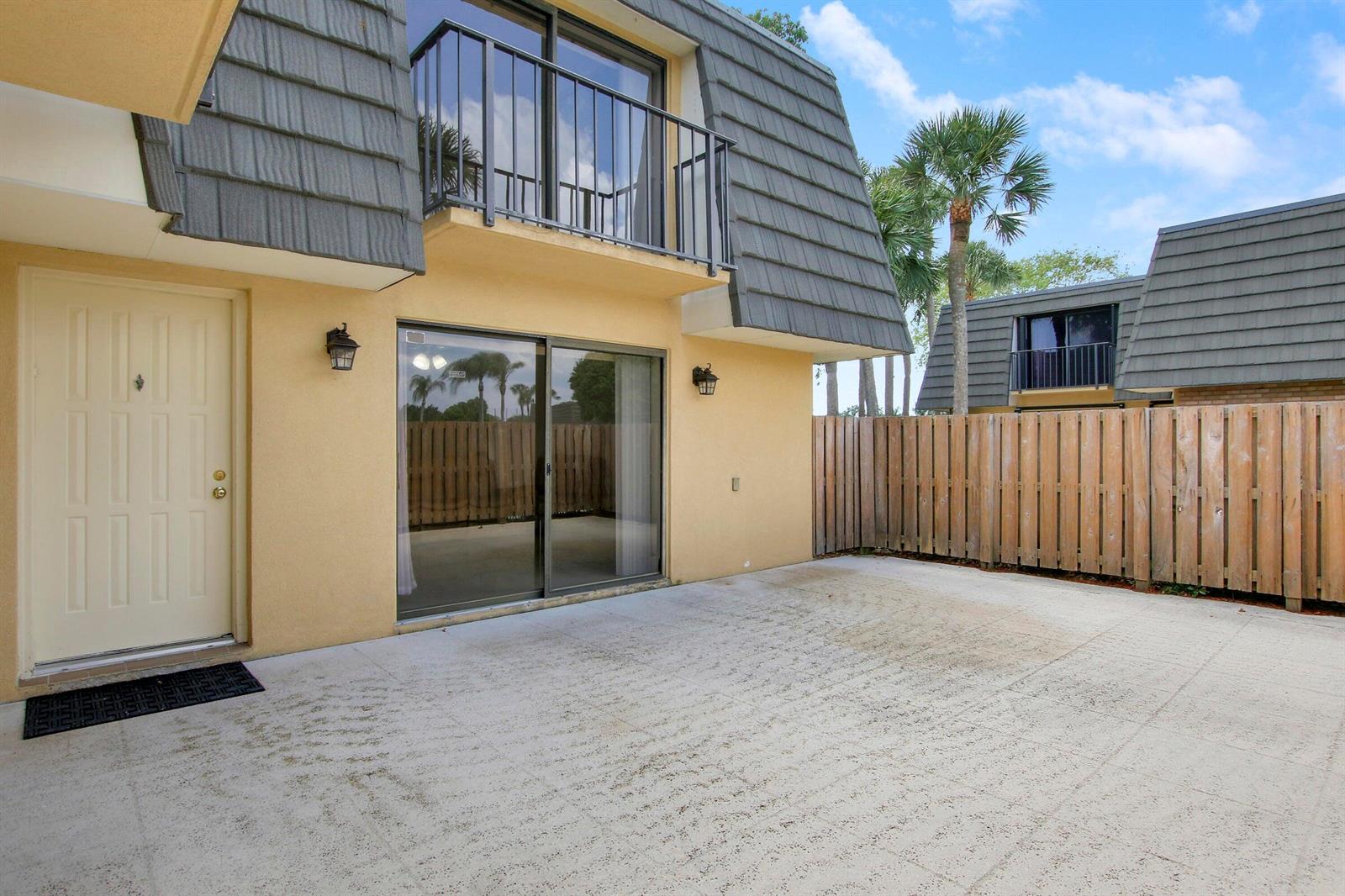 A concrete patio sits outside a tan building with a sliding glass door and balcony — 2404 24th Way, West Palm Beach FL 33407, WEST PALM BEACH, FL