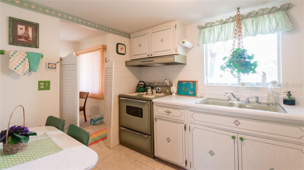 A kitchen features white cabinets, a vintage green stove, and a window with a valance — 1816 SUNNY DRIVE UNIT D21, BRADENTON, FL