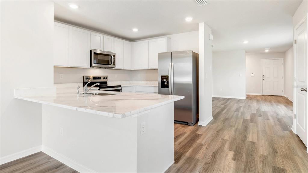 A kitchen with white cabinets and stainless steel appliances opens into a living area — 9984 MORNING MEADOWLARK TRAIL, PARRISH, FL