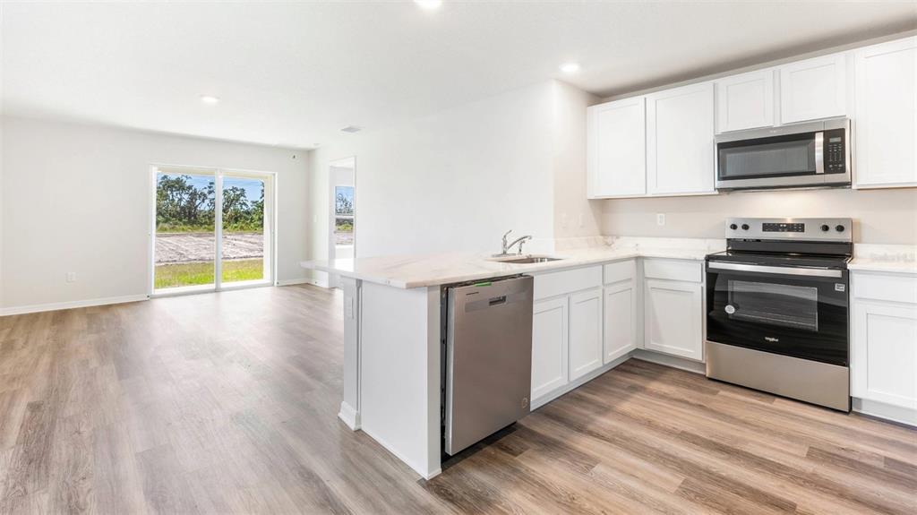 A modern kitchen features white cabinets, stainless steel appliances, and a quartz-topped island with stools — 9984 MORNING MEADOWLARK TRAIL, PARRISH, FL