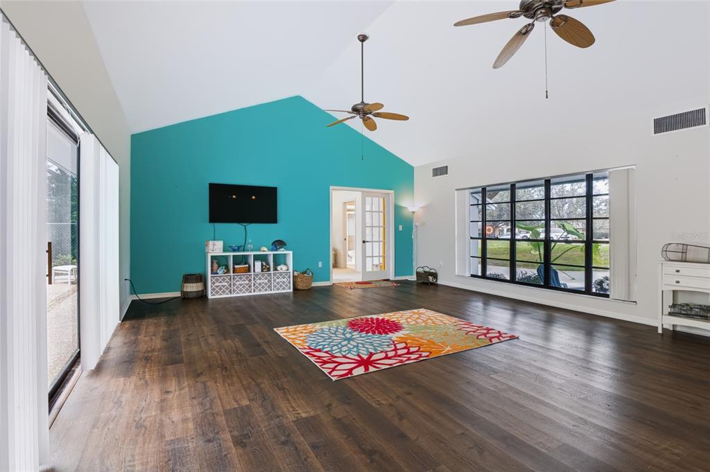 A living room features dark wood floors, a vaulted ceiling, and a bright teal accent wall — 34007 SABAL WAY, LEESBURG, FL
