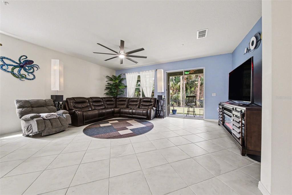A living room features tile flooring, a brown sectional sofa, and a television on a stand — 7646 TURCHETTA COURT, TITUSVILLE, FL