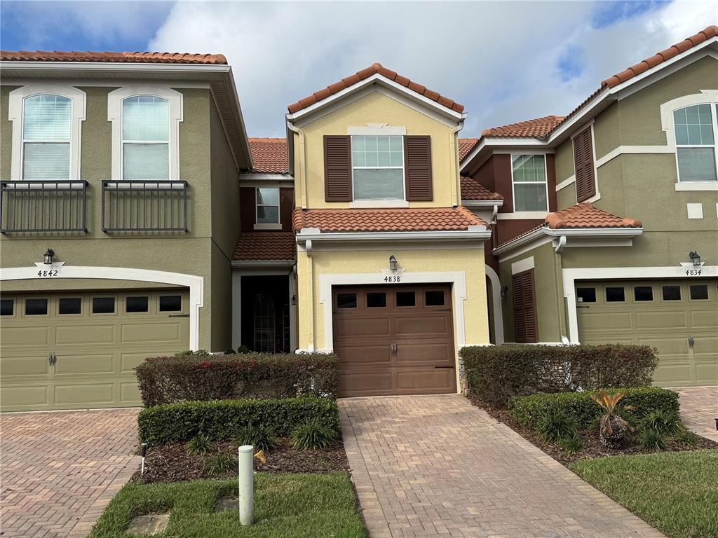 A row of three attached townhomes with stucco facades, tile roofs, and paved driveways — 4838 MATTEO TRAIL, ORLANDO, FL