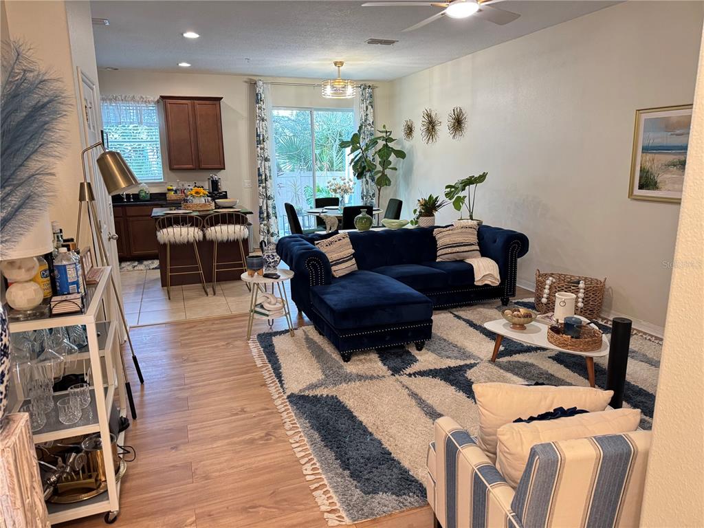 An open-concept living room features a blue velvet sectional, a patterned rug, and a kitchen — 4838 MATTEO TRAIL, ORLANDO, FL