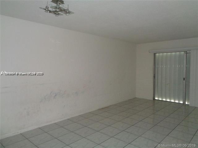 An empty room with white walls, tiled flooring, a ceiling light fixture, and sliding glass doors — 15225 NE 6th Ave # B207, Miami FL 33162, MIAMI, FL