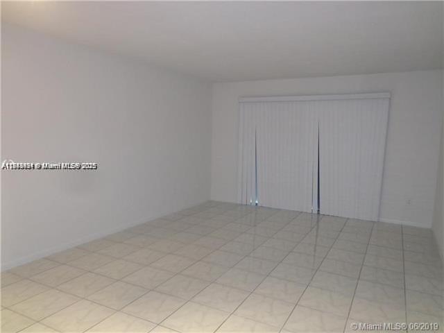An empty room with white walls and light-colored tile flooring features vertical window blinds — 15225 NE 6th Ave # B207, Miami FL 33162, MIAMI, FL