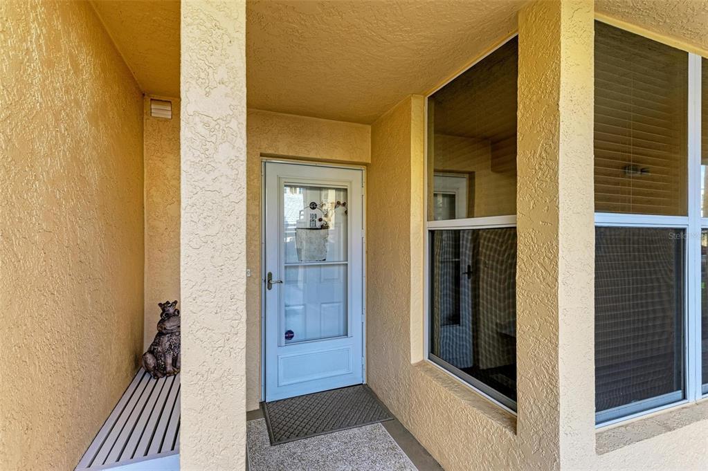A covered entryway features a white storm door, a small frog statue, and windows — 4480 FAIRWAYS BOULEVARD UNIT 109, BRADENTON, FL