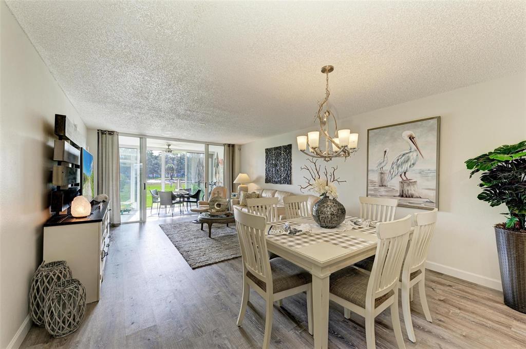 A dining area and living room with wood-look flooring, a chandelier, and a sliding glass door — 4480 FAIRWAYS BOULEVARD UNIT 109, BRADENTON, FL