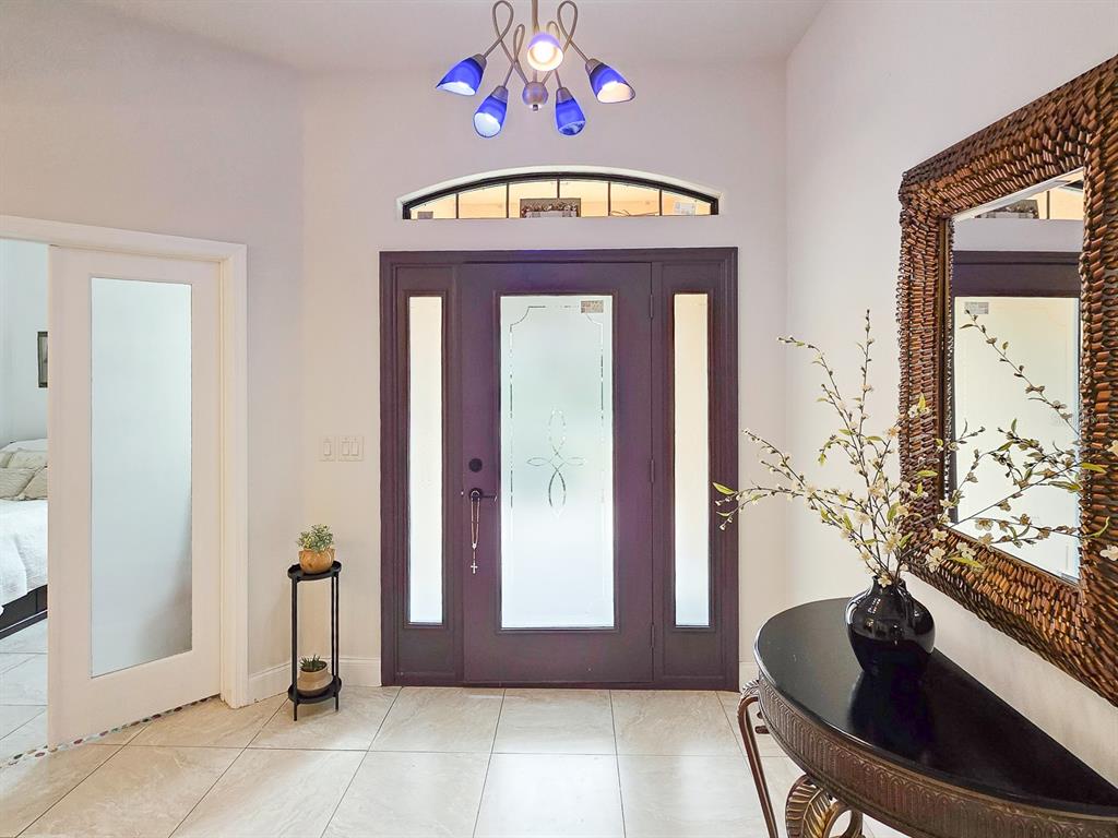 An entryway features a dark purple front door, tiled floors, a chandelier, and a mirror — 13 RIVER OAKS WAY, PALM COAST, FL