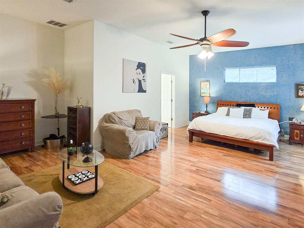 A spacious bedroom features hardwood floors, a blue accent wall, and a seating area — 13 RIVER OAKS WAY, PALM COAST, FL