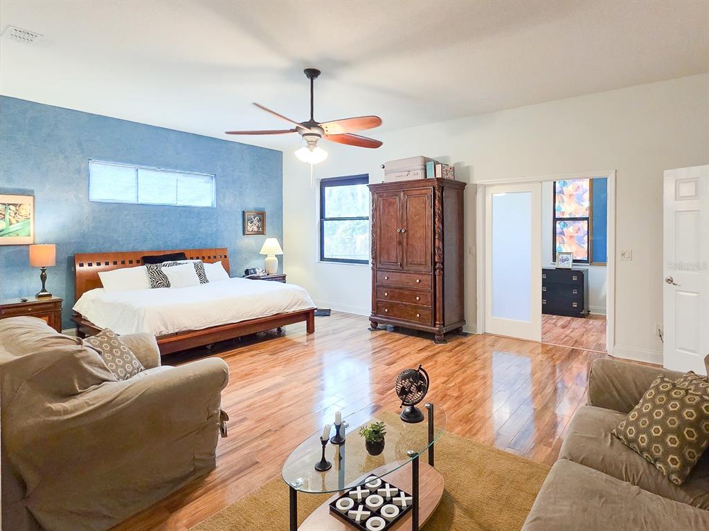 A bedroom with a blue accent wall, hardwood floors, a ceiling fan, and seating area — 13 RIVER OAKS WAY, PALM COAST, FL