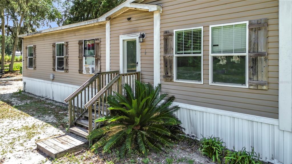 The exterior of a tan mobile home features a wooden staircase and a large plant — 1689 NE 189TH LANE, CITRA, FL
