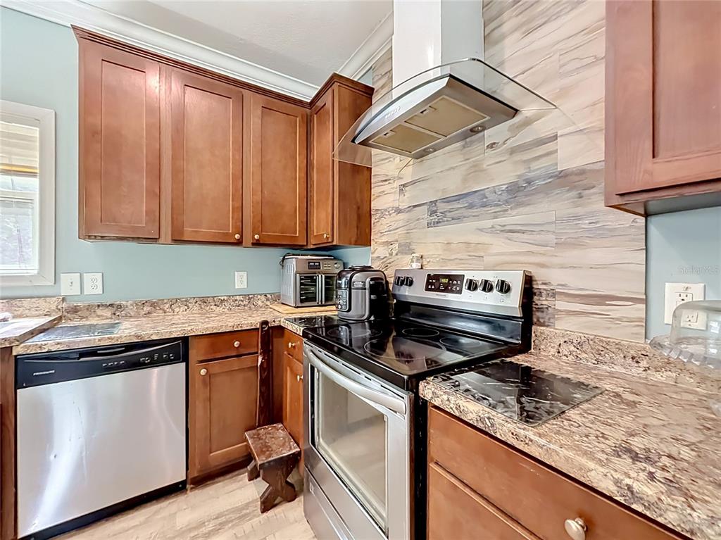 A kitchen features wood cabinets, granite countertops, stainless steel appliances, and a wood-look backsplash — 1689 NE 189TH LANE, CITRA, FL