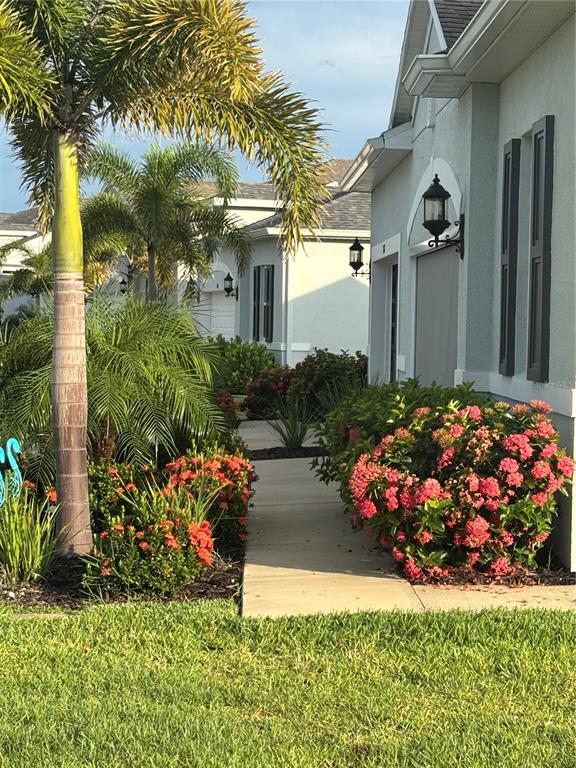 A concrete walkway leads past a palm tree and flowering shrubs toward a house exterior — 1867 NOTTINGHAM TRAIL, PUNTA GORDA, FL