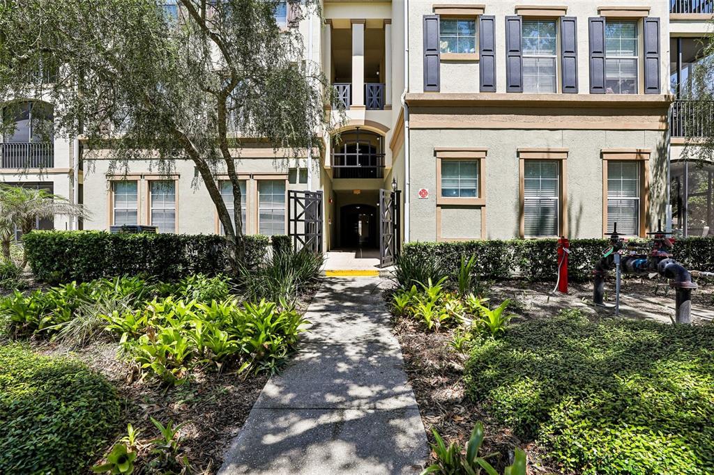 A concrete walkway leads to the entrance of a multi-story apartment building with landscaping — 11564 MIZZON DRIVE UNIT 102, WINDERMERE, FL