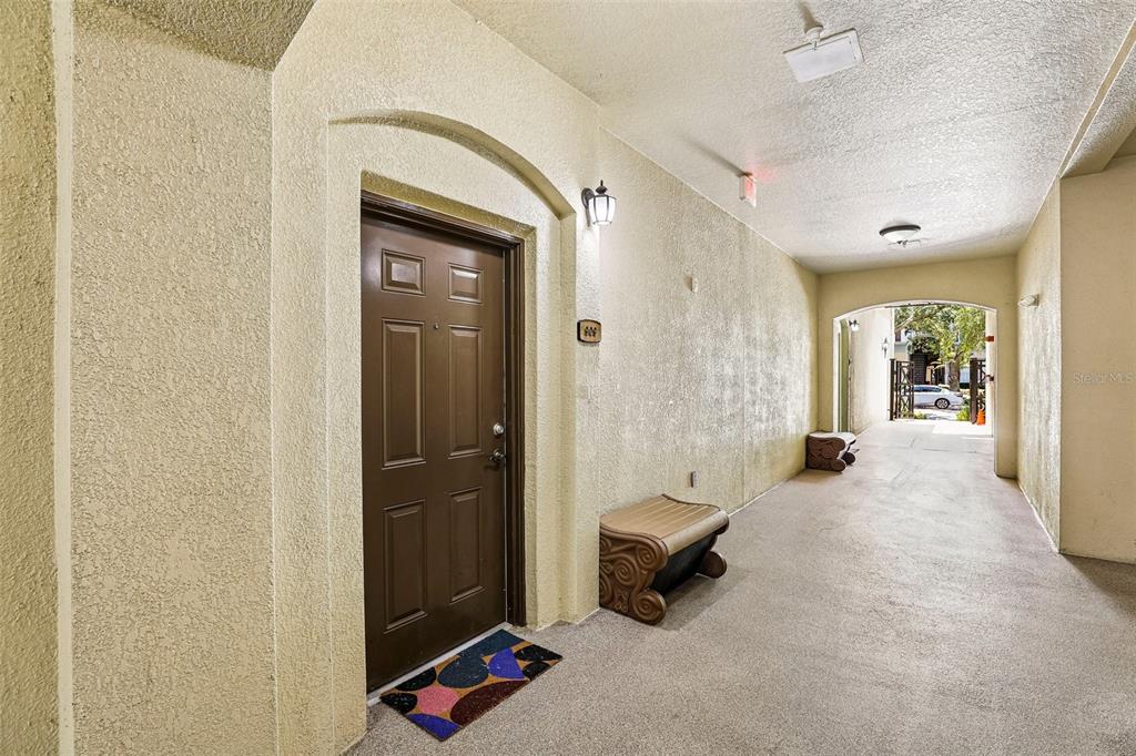 A brown door with a textured wall and a small bench in a covered hallway — 11564 MIZZON DRIVE UNIT 102, WINDERMERE, FL