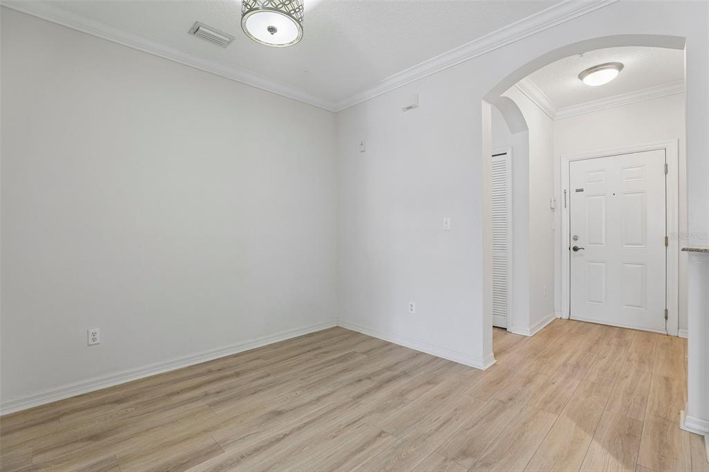 An empty room with light wood-look flooring, white walls, crown molding, and an arched entryway — 11564 MIZZON DRIVE UNIT 102, WINDERMERE, FL