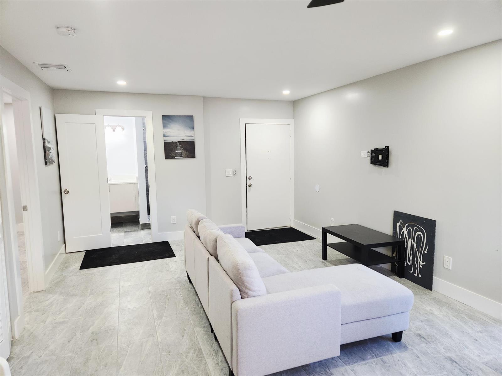 A living room features light gray tile flooring, a sectional sofa, and a wall-mounted television bracket — 2050 Oleander Boulevard # 109, Fort Pierce FL 34950, FORT PIERCE, FL
