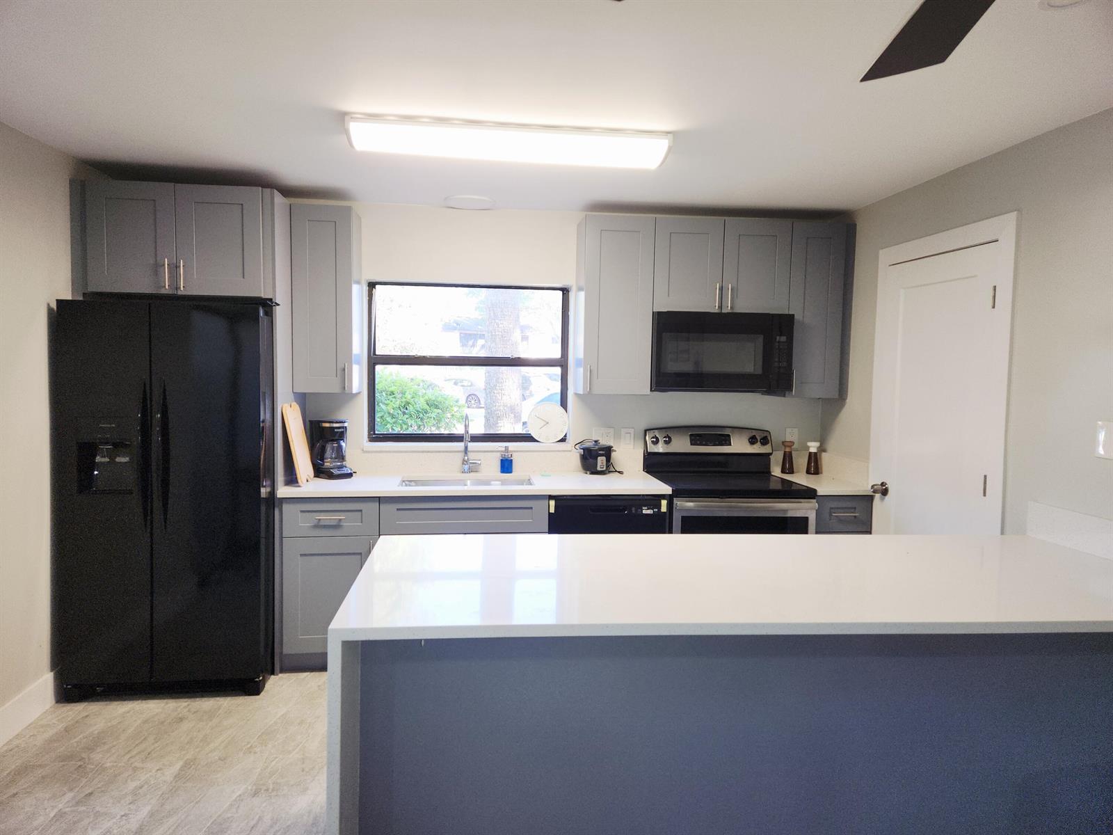 A kitchen features gray cabinets, black appliances, white countertops, and a large island — 2050 Oleander Boulevard # 109, Fort Pierce FL 34950, FORT PIERCE, FL