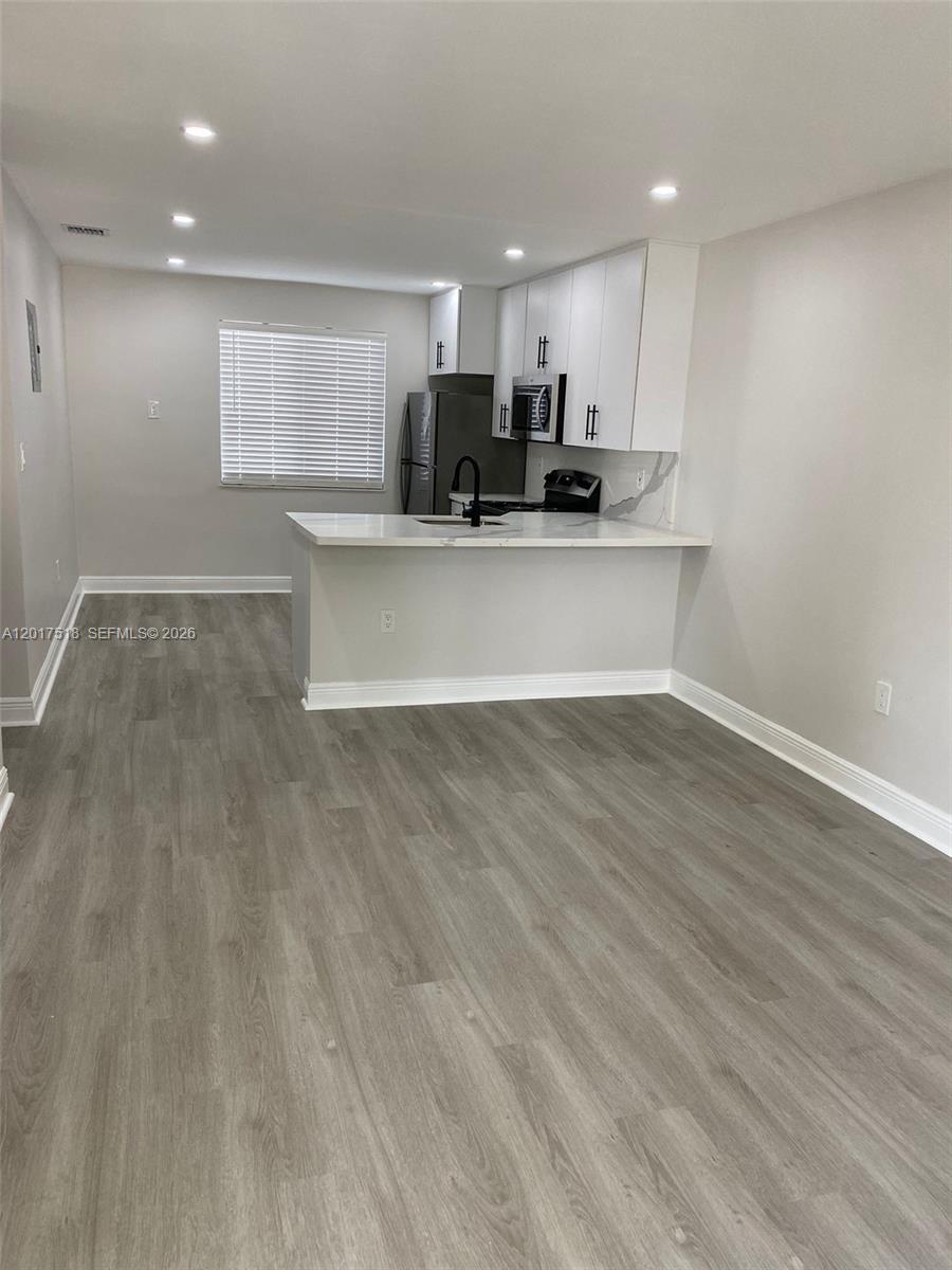 A kitchen with white cabinets and a peninsula overlooks a living area with gray flooring — 4650 W Flagler St # 3, Miami FL 33134, MIAMI, FL
