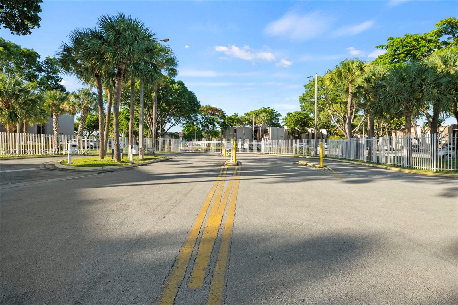 A paved driveway leads to a gated entrance surrounded by palm trees and white fencing — 3581 SW 117th Ave # 206, Miami FL 33175, MIAMI, FL