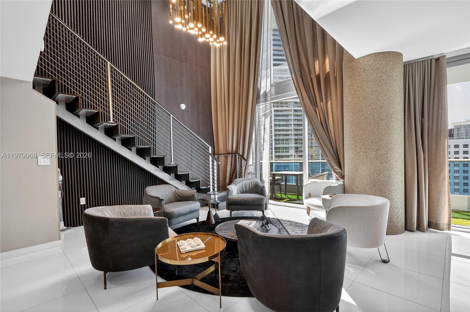A modern living room features a floating staircase, floor-to-ceiling windows, and a circular seating arrangement — 200 Biscayne Boulevard Way # 1108, Miami FL 33131, MIAMI, FL