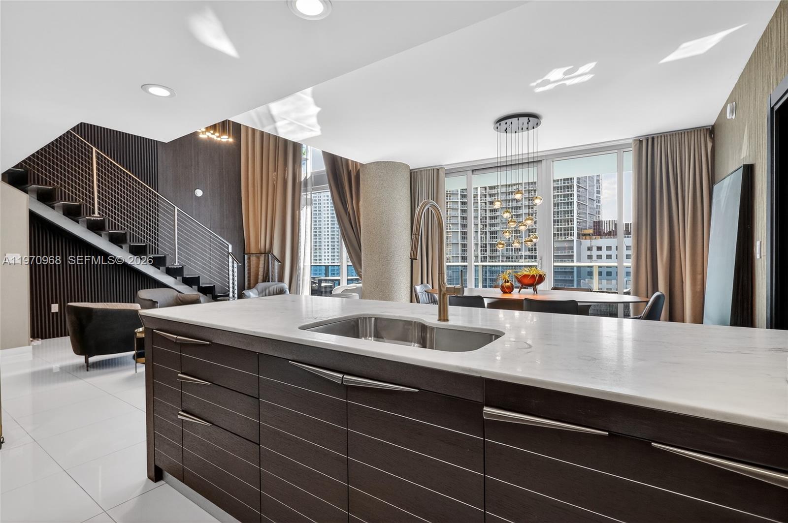 A modern kitchen island with a marble countertop sits before a dining area and staircase — 200 Biscayne Boulevard Way # 1108, Miami FL 33131, MIAMI, FL
