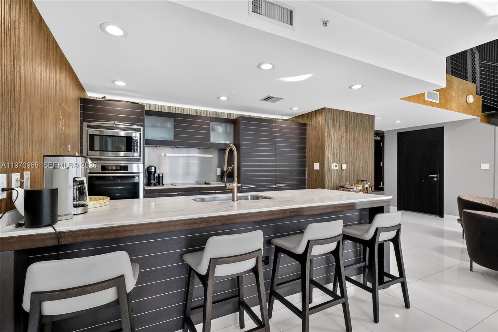 A modern kitchen features dark wood cabinetry, a marble-topped island, and four bar stools — 200 Biscayne Boulevard Way # 1108, Miami FL 33131, MIAMI, FL