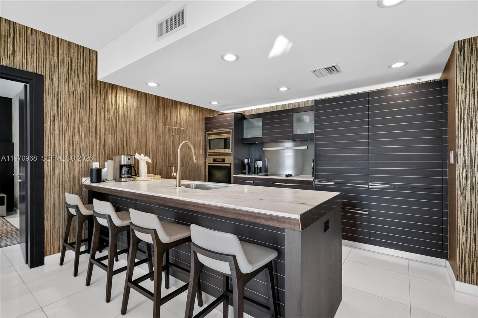 A modern kitchen features a stone-topped island with bar seating and dark horizontal-slatted cabinetry — 200 Biscayne Boulevard Way # 1108, Miami FL 33131, MIAMI, FL