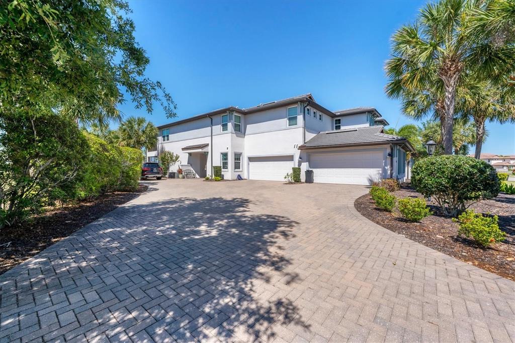 A two-story house with a paved driveway, three-car garage, and surrounding palm trees — 7564 DIVOT LOOP, BRADENTON, FL