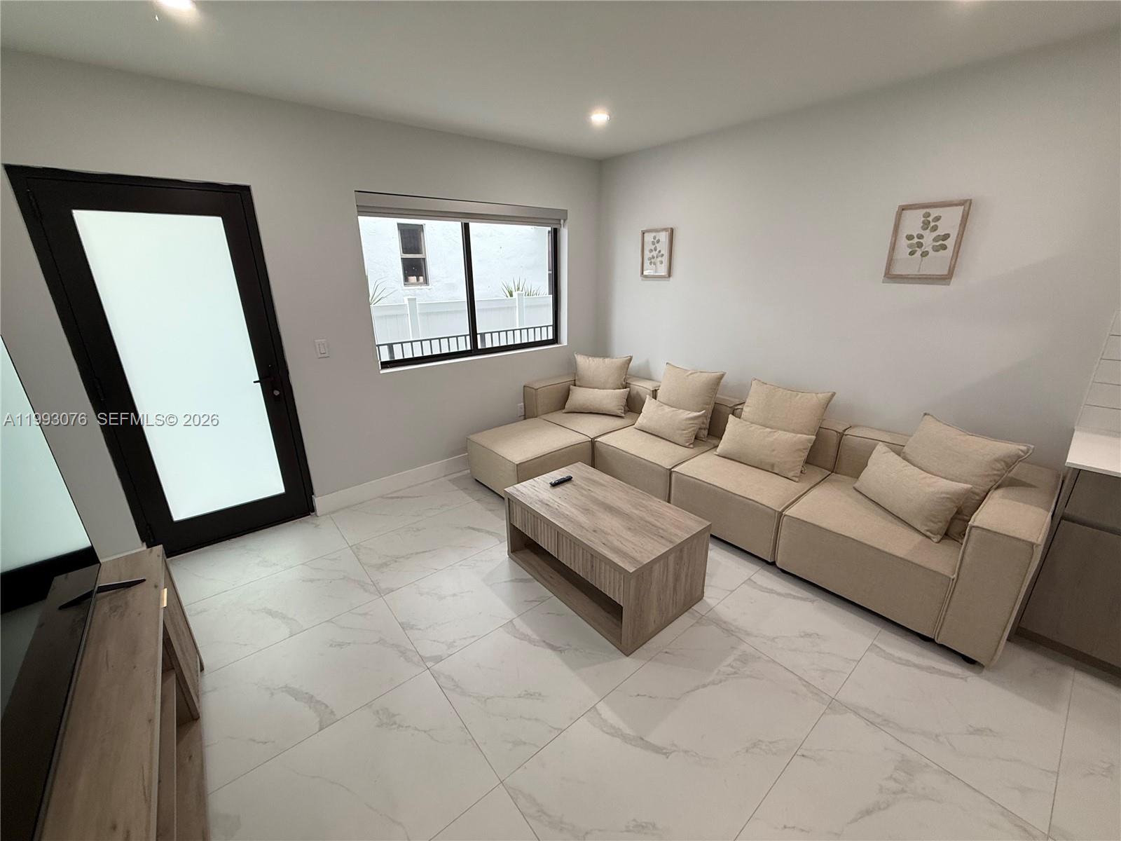 A living room features a beige sectional sofa, a wood coffee table, and tiled floors — 944 Jefferson Ave # 15, Miami Beach FL 33139, MIAMI BEACH, FL