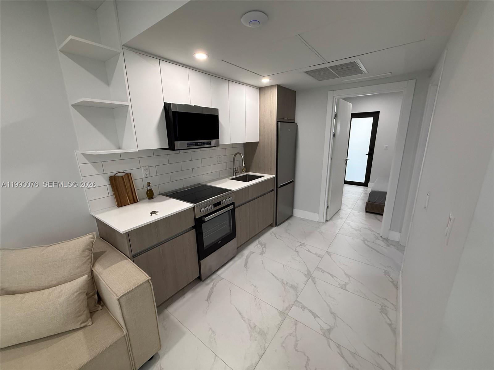 A modern kitchen features white upper cabinets, wood-tone lower cabinets, stainless steel appliances, and marble-look flooring — 944 Jefferson Ave # 15, Miami Beach FL 33139, MIAMI BEACH, FL