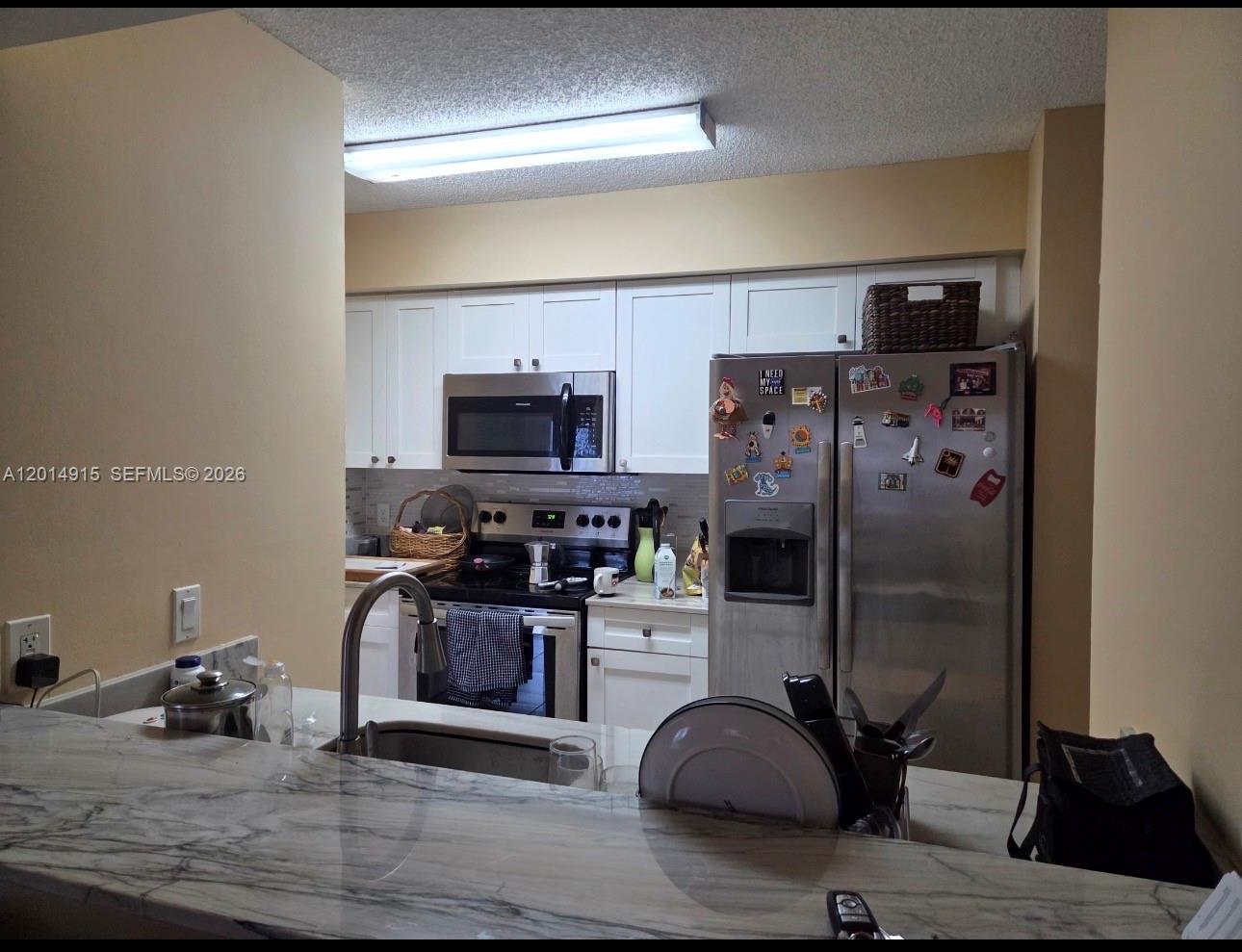 A kitchen features white cabinets, stainless steel appliances, and a marble-patterned countertop on the island — 520 S Park Rd # 12, Hollywood FL 33021, HOLLYWOOD, FL