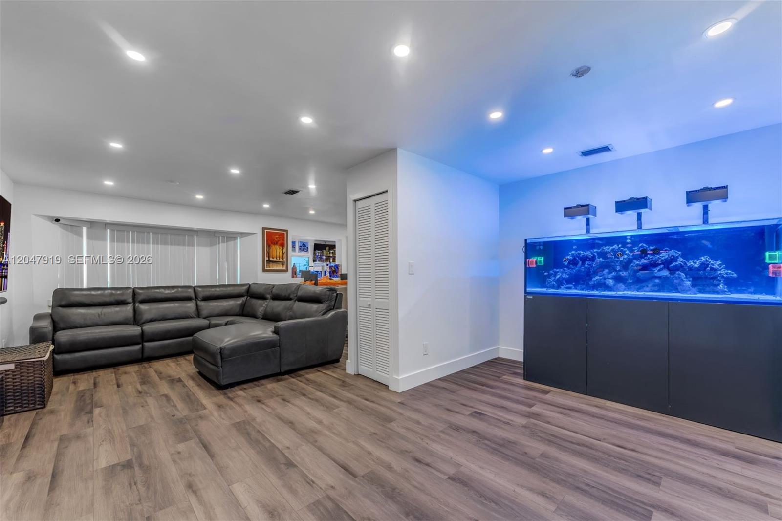 A living room features wood-look flooring, a gray sectional sofa, and a large built-in aquarium — 13770 SW 192nd St, Miami FL 33177, MIAMI, FL