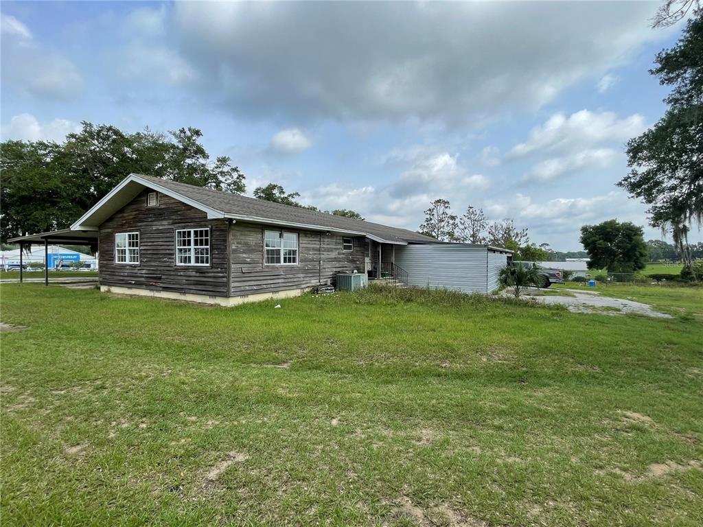 A weathered, single-story wood-sided house sits on a grassy lot under a cloudy sky — 10736 US HIGHWAY 301, DADE CITY, FL