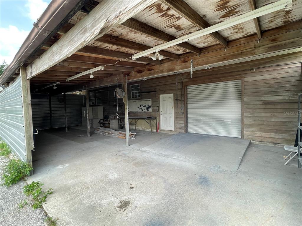 A covered outdoor workspace features a concrete floor, wooden walls, and a roll-up garage door — 10736 US HIGHWAY 301, DADE CITY, FL