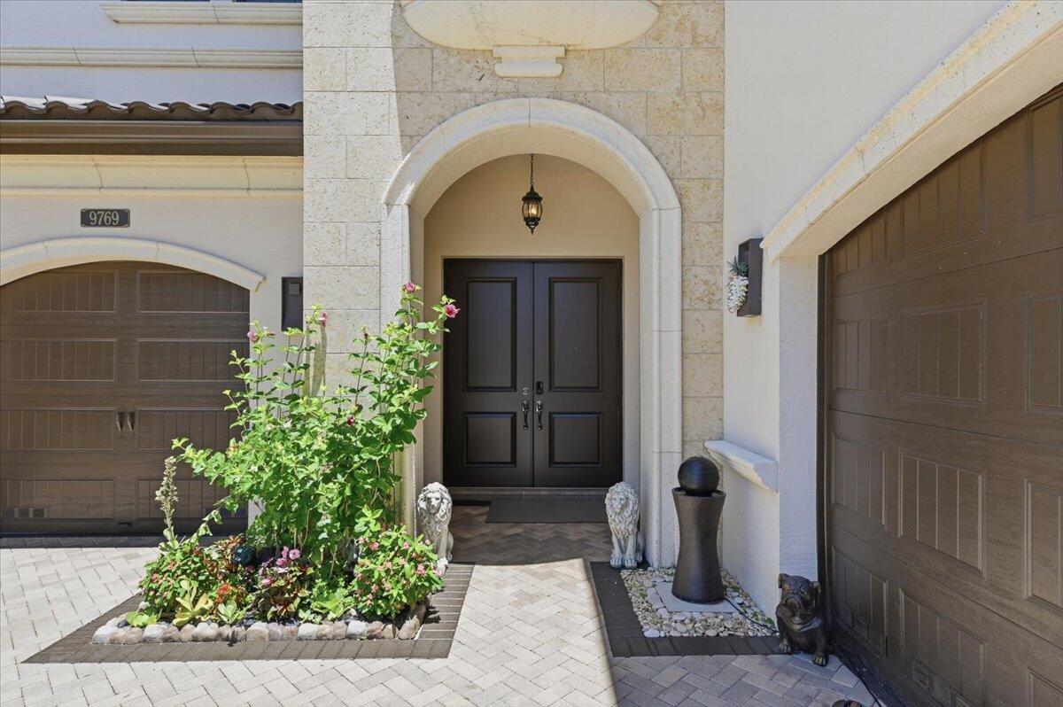 The exterior of a home features a double front door, stone archway, and two garages — 9769 Bozzano Drive, Delray Beach FL 33446, DELRAY BEACH, FL